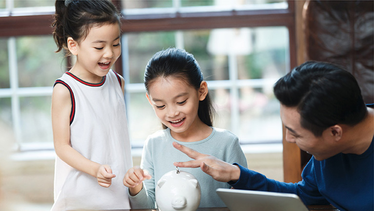 Father and daughters putting money in piggy bank